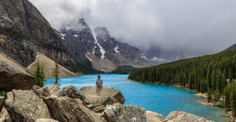 A lone girl sits on a pile of rocks overlooking Moraine Lake in Banff National Park